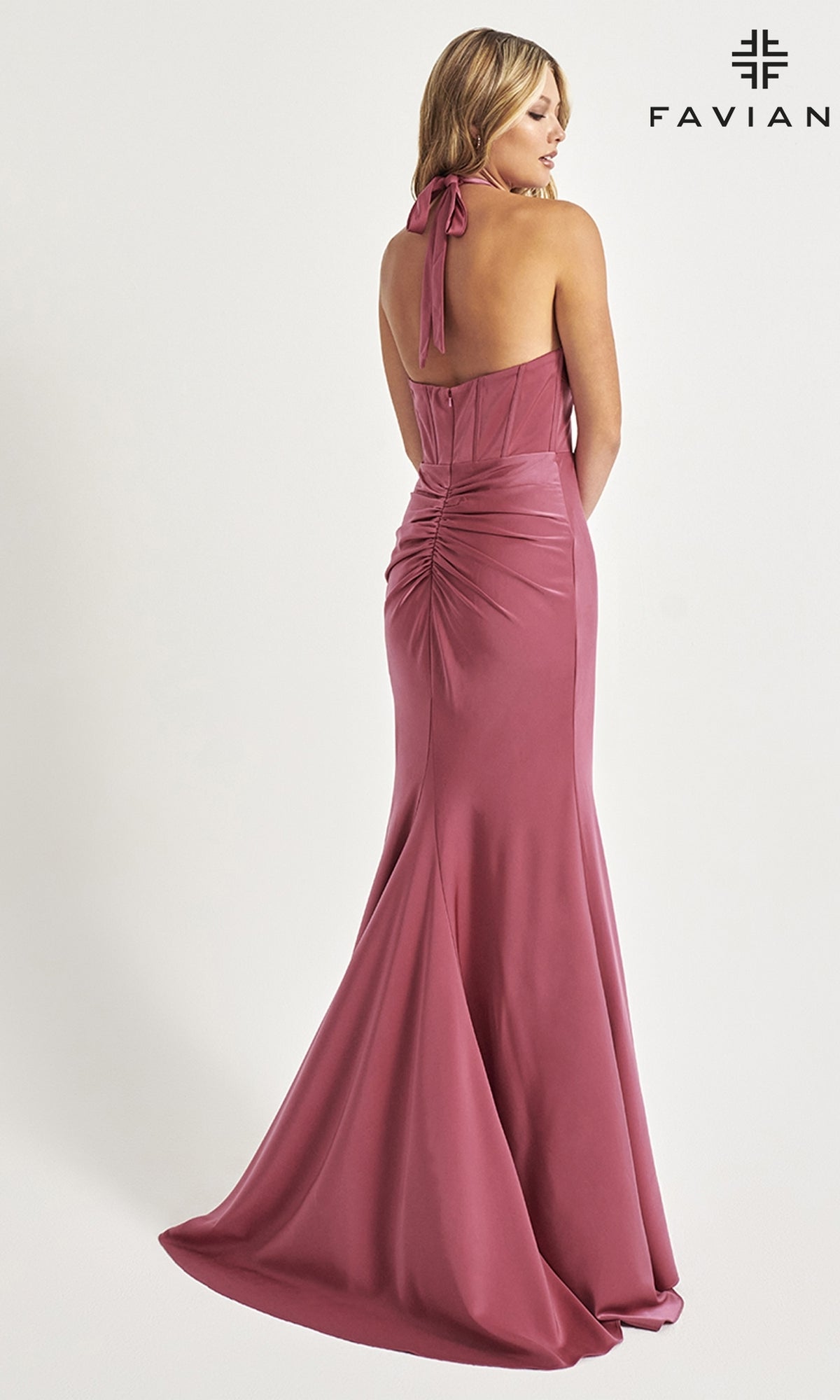 A woman models the Faviana Corset-Waist Long Halter Prom Dress 11065, a floor-length mauve satin gown with a backless design and ruched detailing, standing before a white background with the Faviana logo.